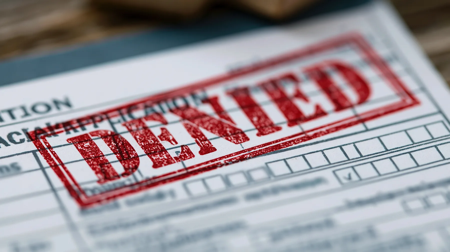 Close-up of a paper application form stamped DENIED in red ink across the checkboxes.